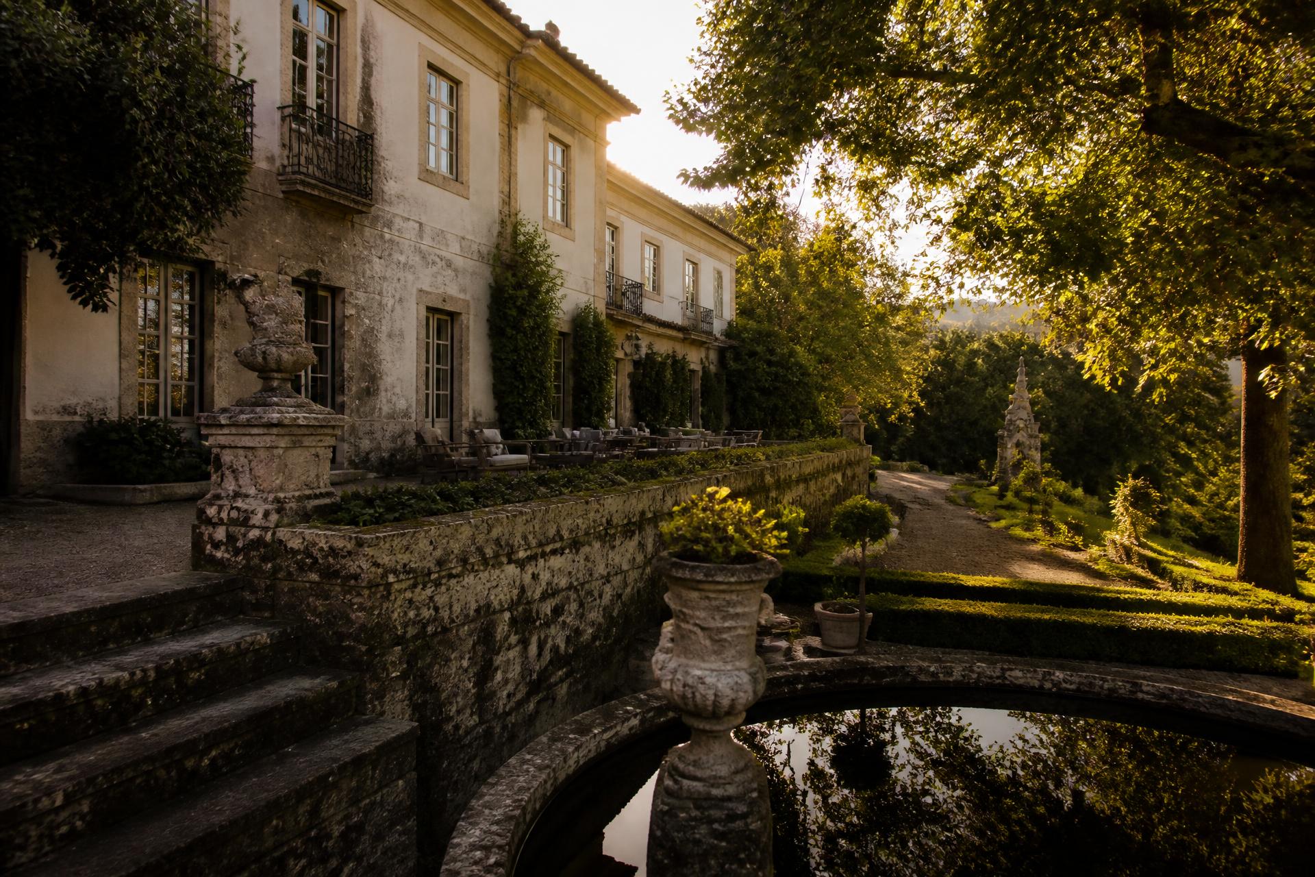 Fachada da Quinta da Mota ao entardecer, envolta em jardins e pedra